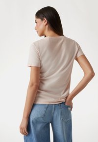 Camiseta de manga corta, rosa, con escote redondo, textura suave y forma ajustada, combinada con pantalones de mezclilla de tiro alto en azul.