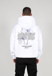 Weißer Hoodie mit einem großen Grafikdesign auf der Rückseite, das lila Schmetterlinge und schwarz stilisierten Text zeigt. Das Material wirkt weich und dick.