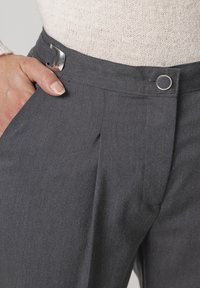 Pantalones grises de corte ajustado con un frente plano, que cuentan con un broche de metal y un detalle de botón circular en la cintura. Textura de tejido suave.