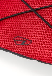 Rotes Netzgewebe mit einem hexagonalen Muster, versehen mit schwarzen Akzenten und einem stilisierten Logo. Die Textur wirkt atmungsaktiv und leicht.