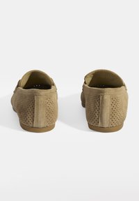 Braune Wildleder Slipper mit perforiertem Design, strukturiertem Obermaterial, abgerundeter Zehenpartie und flacher Gummisohle, von hinten betrachtet.