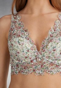 Florale kant bralette met een zachte, romige basis; heeft geschulpte randen, ingewikkelde bloemenpatronen in roze en groen, en een V-hals ontwerp.