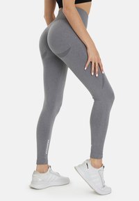 Grijze high-waisted leggings met een gladde textuur, voorzien van een subtiel ontwerp op de achterkant en witte "SQUATPROOF" tekst op het been.