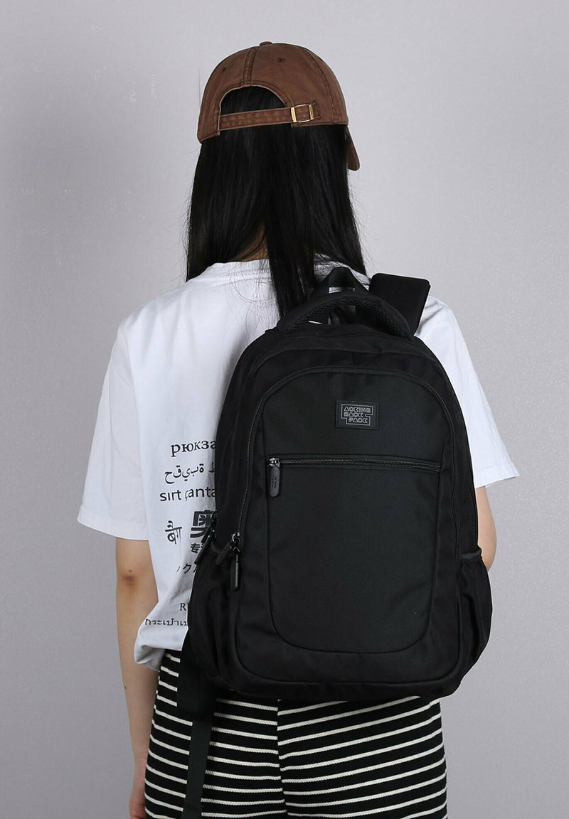 Zwarte rugzak van duurzaam materiaal, met een voorzak met rits, verstelbare schouderbanden en een handvat aan de bovenkant. Heeft een gladde textuur en een minimalistisch ontwerp.