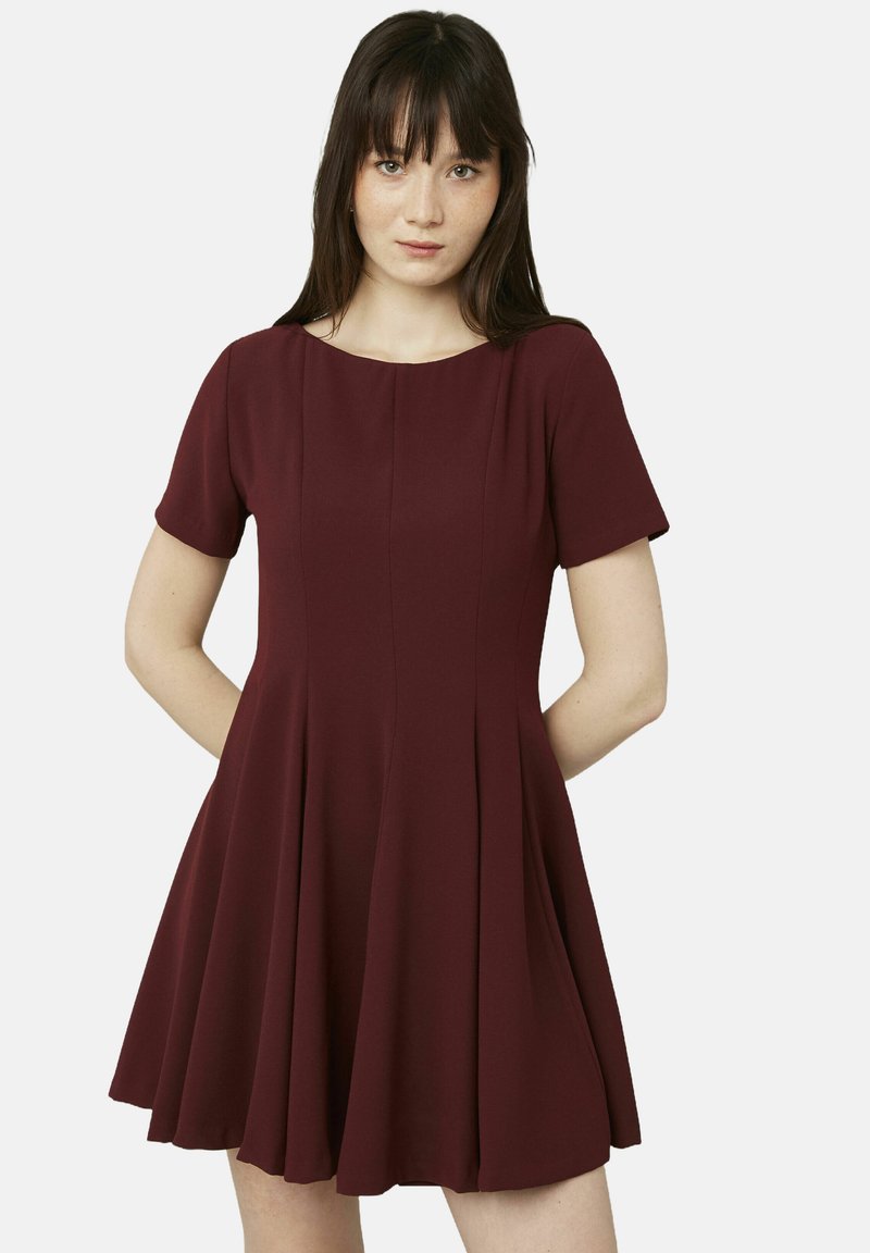 Robe bordeaux à manches courtes avec un corsage ajusté et une jupe évasée. Fabriquée en tissu lisse avec des coutures verticales pour la structure.