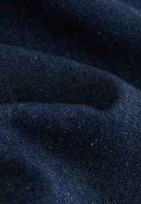 Dunkelblauer Denim-Stoff mit glatter Textur, der ein dezentes Webmuster und kleine Einsprengsel hellblauer Fäden aufweist.