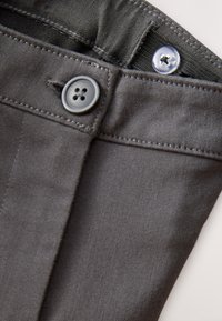 Grijze stoffen broek met een knoopsluiting met vier gaten, zichtbare stiksels langs de tailleband en een glad, textuurrijk oppervlak.