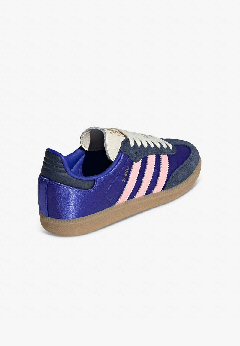 Sneaker featuring a purple upper with navy suede accents, three pink stripes, and a gum outsole. Includes white laces and logo on tongue.