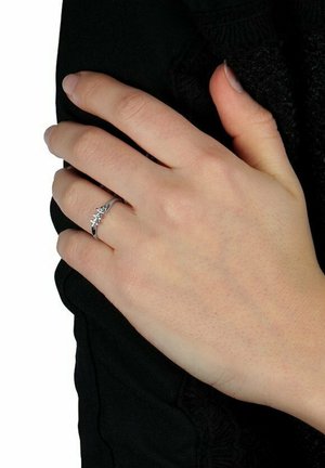 Silberner Ring mit einem geschwungenen Band, versehen mit kleinen, klaren Steinakzenten in einem floralen Design. Am Handgelenk getragen vor einem schwarzen Hintergrund.