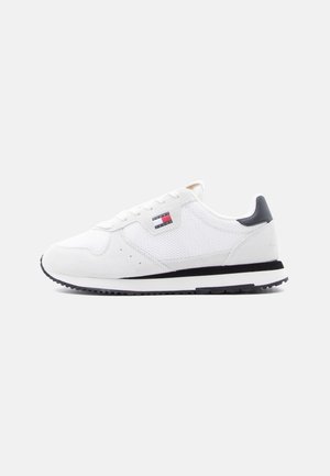 Weißer Sneaker mit niedrigem Schaft, Mesh- und Wildlederdetails, schwarzem Fersenlasche, schwarz-weißer Sohle und kleinem rechteckigem rot-weiß-blauem Logo an der Seite.