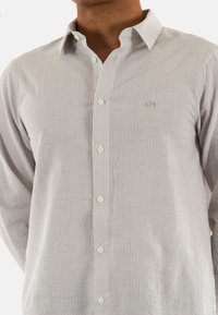 Camicia button-up grigia chiara con sottili righe orizzontali e verticali. Tessuto dalla texture morbida, caratterizzata da una vestibilità slim e colletto.