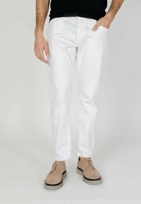 Pantalones de algodón blancos con un diseño de pierna recta, que cuentan con bolsillos laterales y un cierre clásico de cinco botones, combinados con zapatos de ante beige.