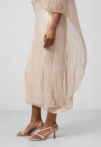 Helles rosa plissee Kleid mit transparenter Textur, lockerer Passform und ausgestellten Ärmeln. Kombiniert mit beigen Sandalen mit Riemchen und flachem Absatz.