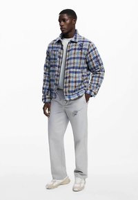 Geruit jasje in blauw, wit en beige materialen, met een kraag en zakken; gecombineerd met lichtgrijze broek en crèmekleurige sneakers.