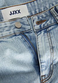 Ljusblå denimjeans med dragkedja, kopparfärgade sömmar och en märkesetikett som läser "JJXX" vid midjan. Silverfärgad knappdetalj.