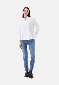 White button-up shirt with a collar, paired with light blue jeans and black ankle boots, against a plain white background.
