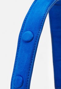 Blå mockarem men med en slät yta och rundade knappar, med kontrasterande sömmar längs kanterna.