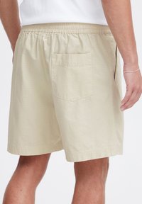 Light beige shorts with an elastic waistband. Features a single back pocket and subtle textured stripes throughout the fabric.