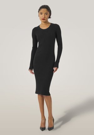 Abito midi a coste nero con maniche lunghe, scollo a barca e silhouette aderente, abbinato a tacchi alti a punta.