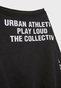 Felpa nera in tessuto morbido con una stampa bianca audace: "URBAN ATHLETIC PLAY LOUD THE COLLECTIVE," esposta in modo prominente.