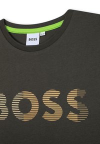 Tmavě šedé tričko s kulatým výstřihem a zeleným lemem, na přední straně s pruhovaným zlatým logem "BOSS". Měkký bavlněný materiál.