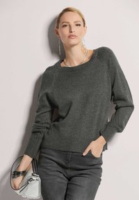 Dunkelgrauer Pullover mit rundem Ausschnitt, gerippten Bündchen und seitlichen Schlitzen, getragen mit schwarzen Jeans und einer silbernen Handtasche.