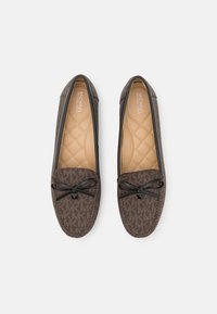 Paire de mocassins marron Michael Kors avec semelles intérieures matelassées couleur fauve, passepoil noir et nœuds noirs décoratifs sur le dessus.