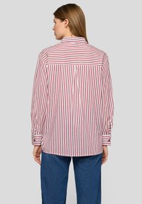 Red and white striped long-sleeve shirt with a classic collar and buttoned cuffs. Features a pleat detail at the back. Worn with blue jeans.