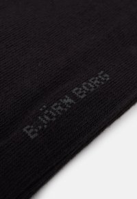 Schwarzer Strickschal mit feiner Textur. Enthält den Markennamen "B.JÖRK BORG", dezent in Grau nahe dem Rand eingestickt.