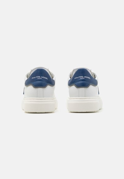 Zapatillas de cuero blanco con acentos en gris y navy, suela de goma texturizada y un logotipo grabado en el talón trasero. Diseño minimalista.