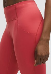 Leggings de tiro alto, ajustados al cuerpo, en poliéster rojo vibrante. Incluyen un bolsillo lateral, costuras planas y una textura suave.