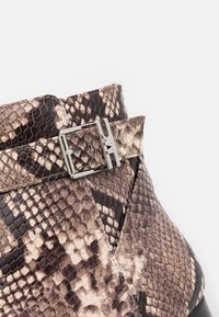 Gros plan d'une botte cheville marron et beige à motif peau de serpent avec une boucle et une lanière argentées.