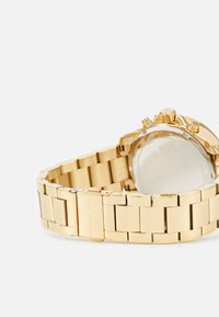 Goldfarbener Edelstahl-Armbanduhr mit einem Gliederarmband, Chronographenfunktionen und klarem Glasrand, mit Branding auf der Rückseite.