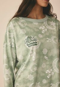 Heled roheline dress, millel on valged poolkuu, tähe ja laterna mustrid. "Ramadan Kareem" tekst dekoratiivses skriptis keskosas.