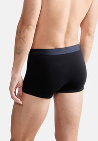 Schwarze Boxershorts mit einem kontrastierenden marineblauen Bund, aus glattem Stoff, enganliegendem Design mit niedrigem Bund und minimalen Nähten.