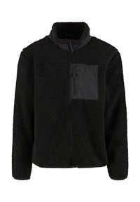 Czarna polarowa kurtka o miękkiej, teksturowanej powierzchni, z wysokim kołnierzem i zapinaną na zamek kieszenią na klatce piersiowej wykonaną z gładkiego materiału.