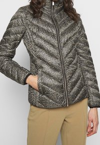 Veste rembourrée avec un imprimé léopard doré et noir, fermeture éclair, col montant, et poignets et ourlet élastiques, fabriquée à partir d'un tissu lisse.