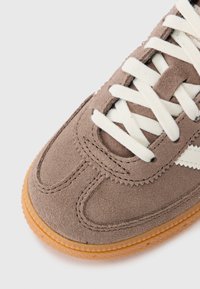 Baskets en daim marron avec des lacets blancs, présentant une surface texturée et une semelle en gomme. Détails de couture contrastante le long de la tige.