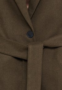 Manteau en laine marron foncé avec un bouton noir et une large ceinture en tissu nouée à la taille, montrant les détails texturés du tissu.