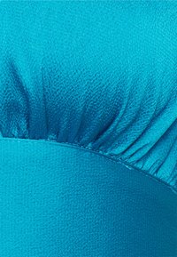 Vestido turquesa com detalhes de tecido franzido na parte superior. Textura suave com uma seção inferior contrastante, ambas em tons vibrantes de azul.