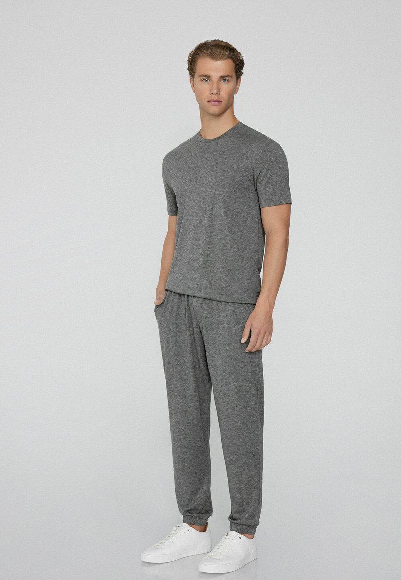 Graues T-Shirt und Sweatpants-Set aus einem weichen, leichten Stoff. Verfügt über einen lockeren Schnitt, ein elastisches Bündchen und gerippte Bündchen. Weiße Sneaker.