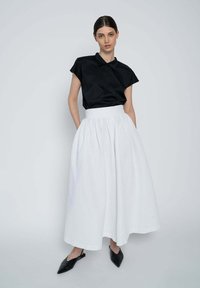 Black short-sleeve top paired with a white, textured, full-length skirt. The outfit features a high waistband and pointed black shoes.