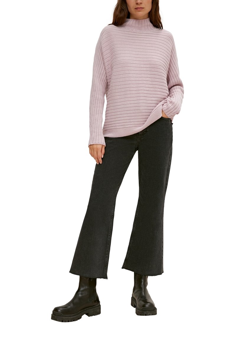 Lichtroze, gestreepte gebreide trui met een hoge hals, gecombineerd met zwarte uitlopende jeans en chunky zwarte enkellaarzen.