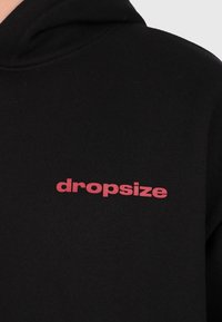 Schwarzer Hoodie mit dem Wort "dropsize", das in fetten roten Kleinbuchstaben auf der Brust gedruckt ist.