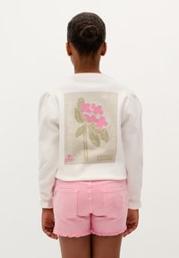 Weißes Sweatshirt mit floraler Grafik in Pink und Grün auf dem Rücken, kombiniert mit hellen, fransigen Jean-Shorts in Rosa. Glatte Textur, lässiges Design.