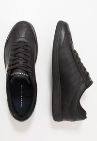 Zwarte leren sneakers hebben een gladde textuur, een platte vetersluiting, een gepolsterde kraag en een logo op de tong en zijkant met subtiele streepaccenten.