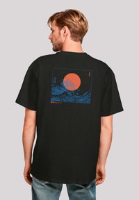 Zwarte katoenen t-shirt met een blauwe grafiek van golven en een oranje zon op de achterkant. Korte mouwen en een ontspannen pasvorm.