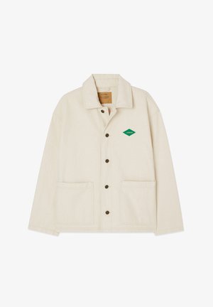 Kreemit värvi jakk, mis on valmistatud vastupidavast kangast, millel on terav krae, nööbiga sulgemine, kaks esiripa ning roheline rombikujuline logo vasakul rinnal.