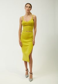 Gelbes Strick-Zweiteiler-Set, bestehend aus einem gerippten Crop-Top und einem knielangen Rock mit einem seitlichen Schlitz, kombiniert mit glitzernden silbernen Absätzen.