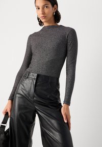 Haut ajusté à manches longues en tissu texturé de couleur gris métallique avec des détails côtelés, associé à un pantalon en cuir noir taille haute.